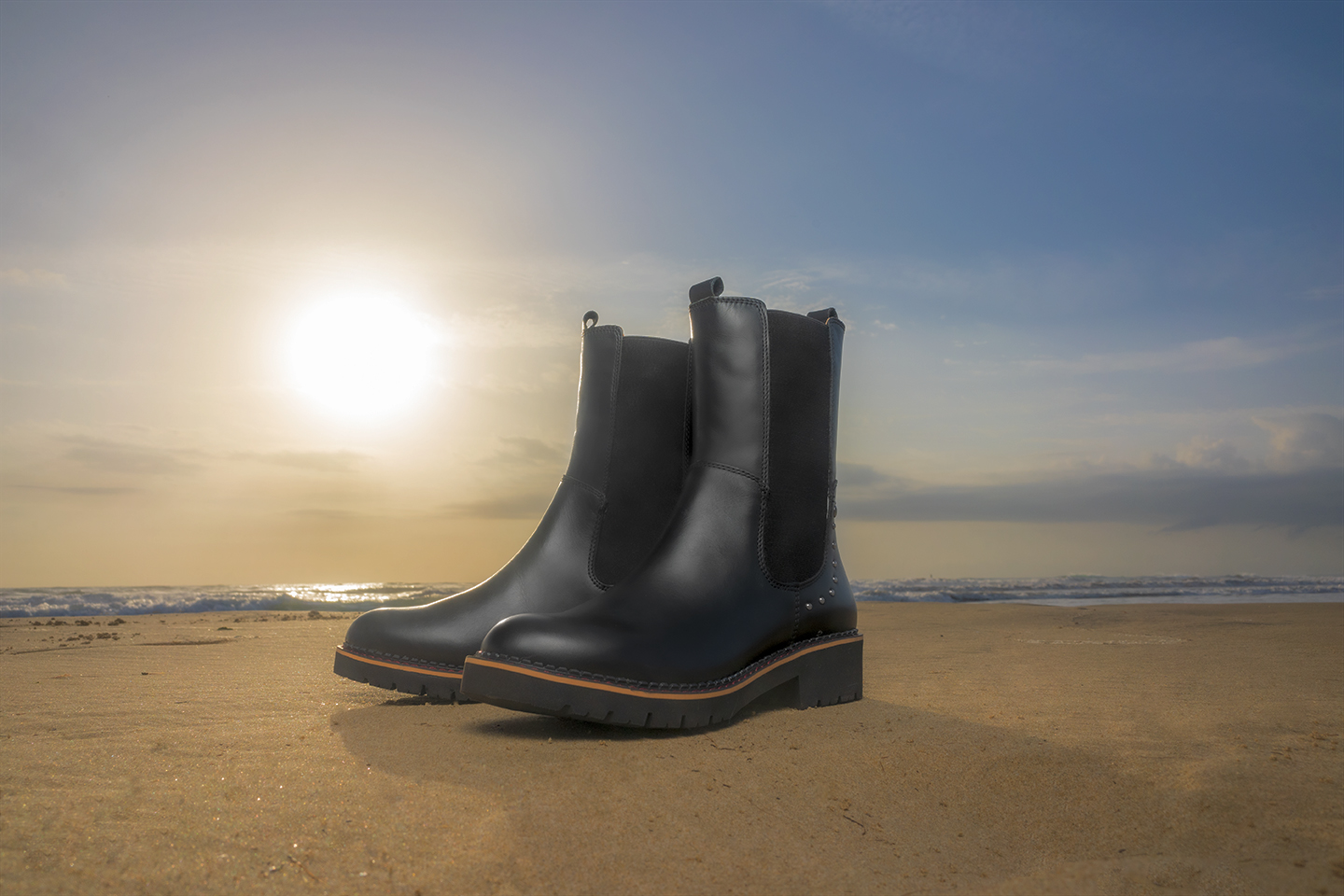 Imagen de unas botas Pikolinos de mujer en color negro en la arena de la playa.
